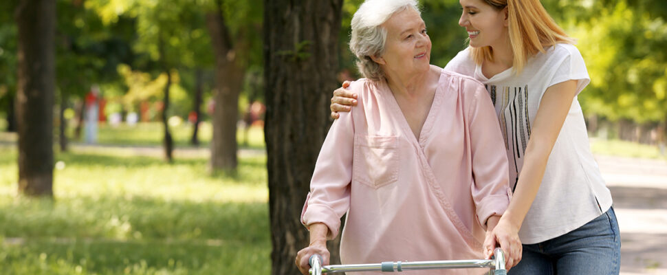 Caretaker helping elderly woman with walking outdoors